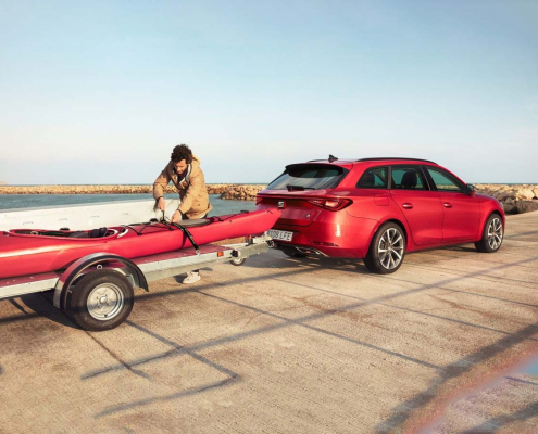 SEAT Leon SUV in red pulling a red boat with a man fixing the boat.