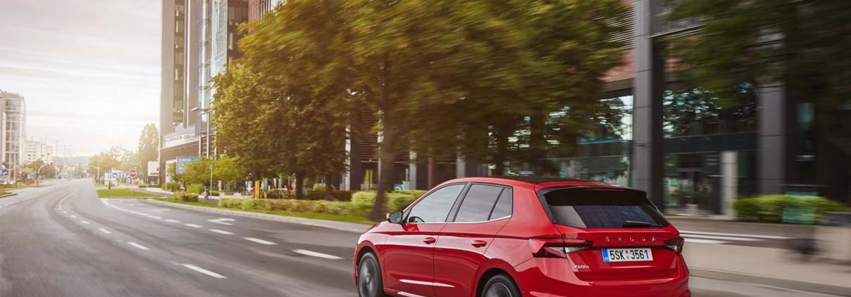 Red ŠKODA FABIA driving through a city.